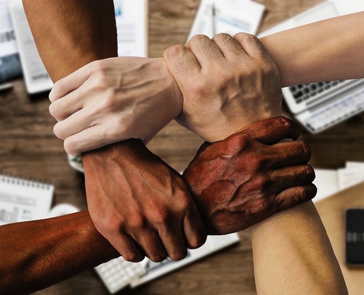 multi-race hands gripping each others wrists to form an interlocked square pattern
